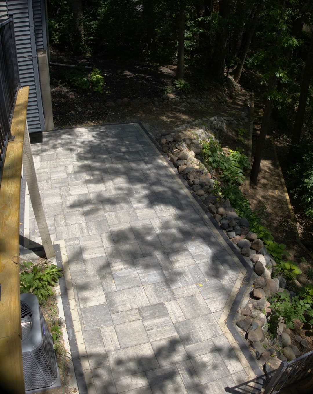 Paved patio area with natural stone border in a wooded backyard setting.