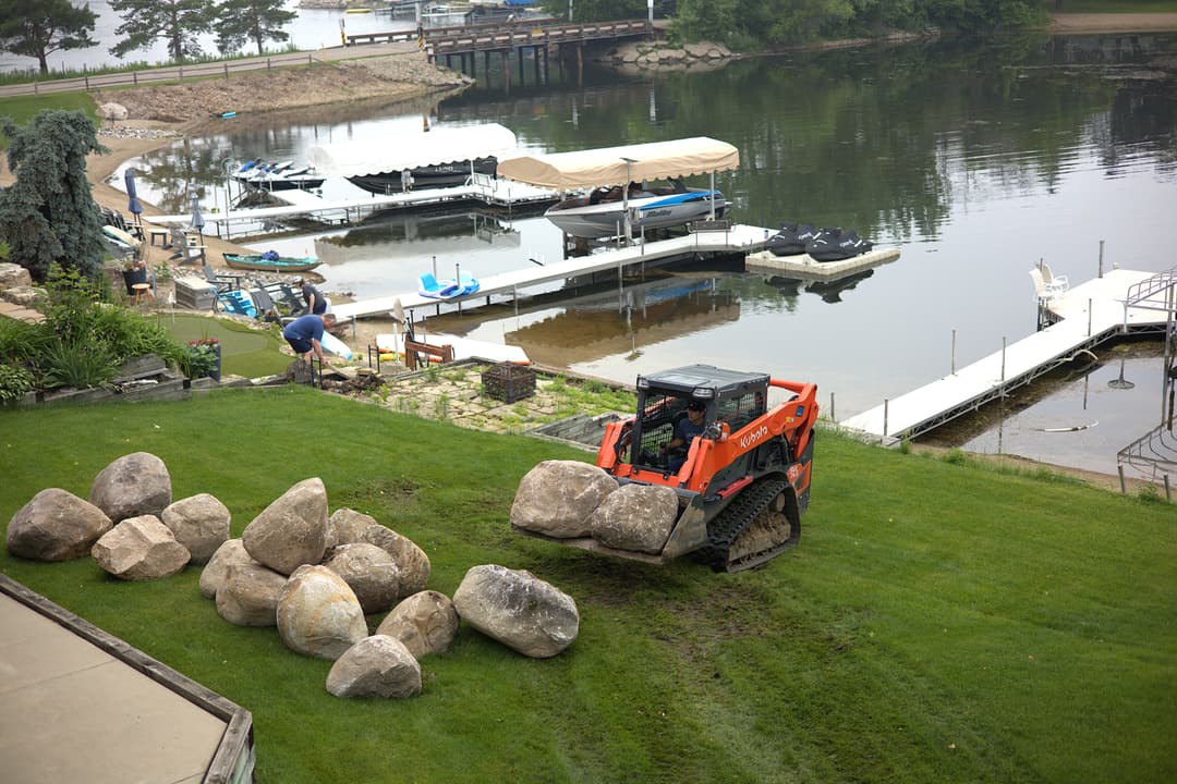 Bobcat landscaping with large rocks near a lakeside dock.