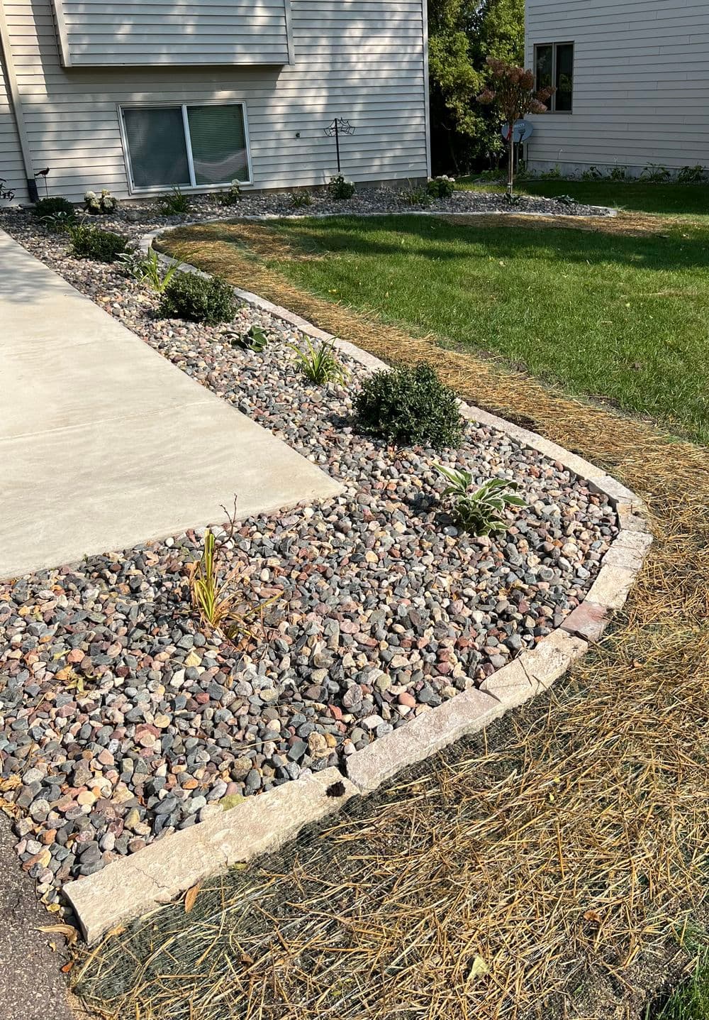 Landscape design featuring decorative stones, plants, and a manicured yard near a home.