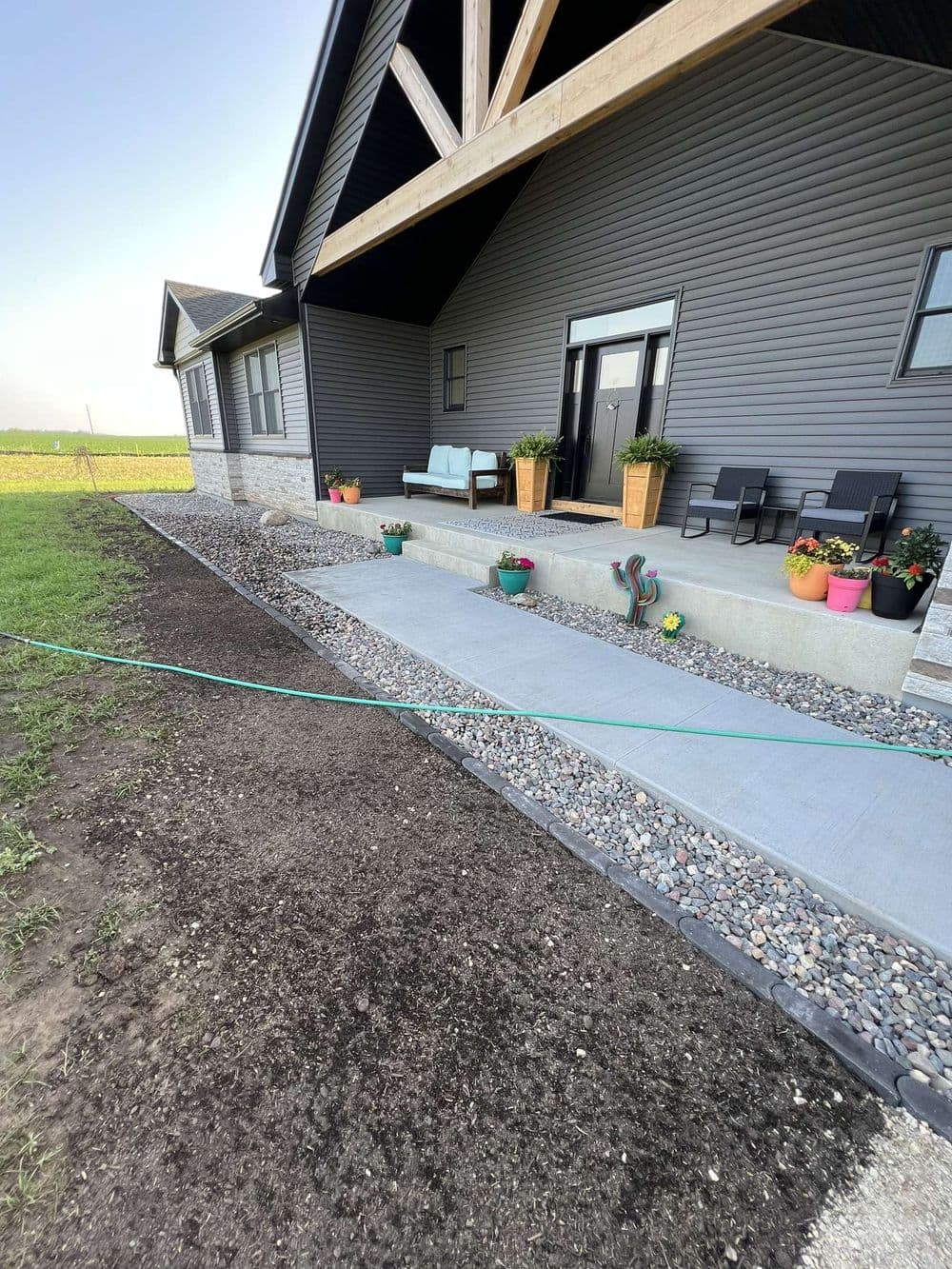 Modern home entrance with patio seating, flower pots, and landscaped gravel path.