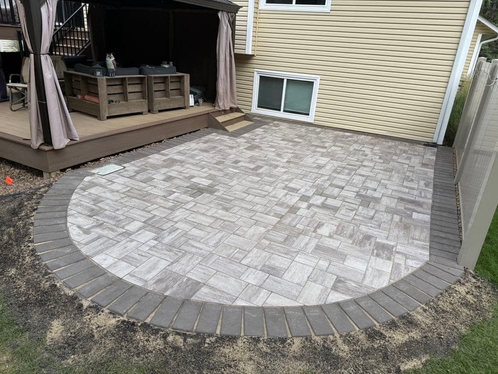 Paved outdoor patio with circular stone border next to home and shaded seating area.