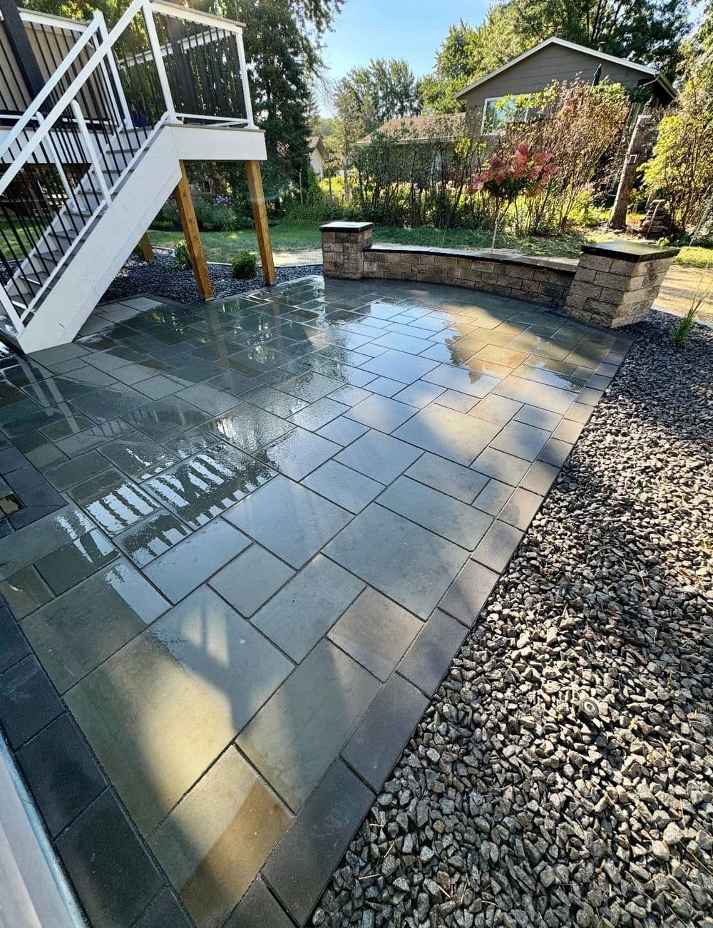 Clean outdoor patio with stone pavers, surrounded by gravel and lush greenery. Ideal for relaxing.
