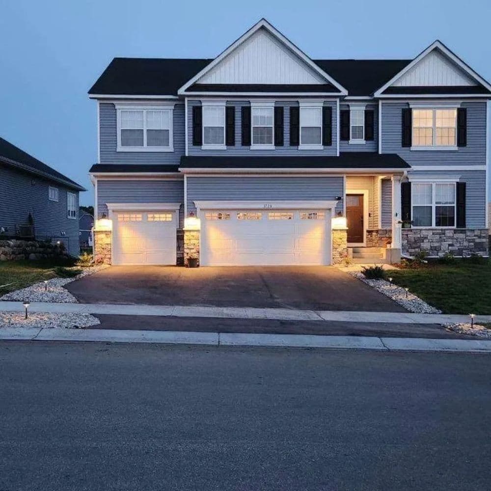 Modern blue two-story house with a three-car garage and landscape lighting at dusk.