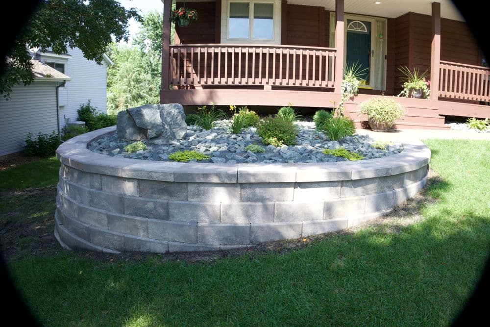 Landscaped garden bed with stone retaining wall and green plants near a house entrance.