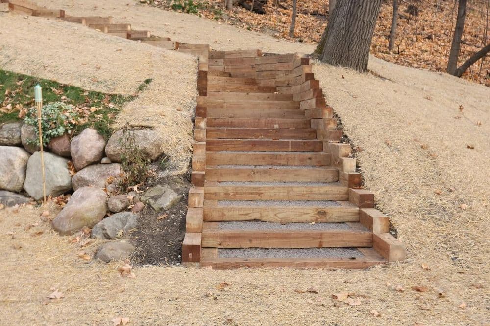 Wooden steps leading up a sloped garden path surrounded by rocks and fallen leaves.