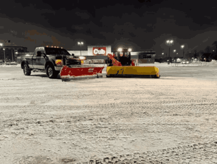 A snow plow is stationed in a parking lot, prepared for snow removal for both commercial and residential areas.