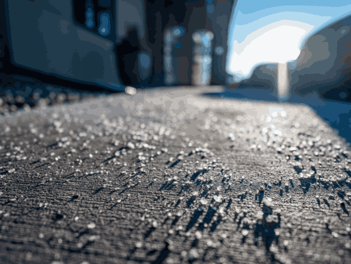Morning water droplets rest on a sidewalk, showcasing the effects of de-icing salt scattered across the surface.