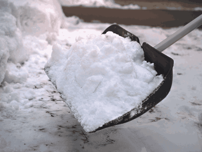 A shovel filled with snow, resting on the ground, indicating the process of shoveling snow.